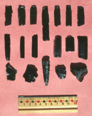 #1-#13, navajas prismáticas de obsidiana; #14-#15, lascas utilizadas de obsidiana; #16, punta de proyectil de obsidiana; #17, lasca no utilizada de obsidiana; #18, núcleo para fabricar lascas de obsidiana.